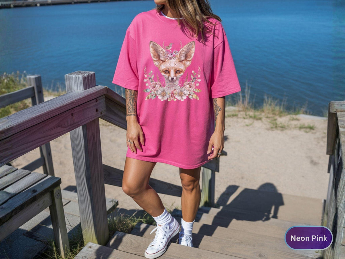 May include: Neon pink oversized t-shirt featuring a fox graphic with floral accents. The fox has a crown and is surrounded by flowers. The shirt is a vibrant pink color and has short sleeves.