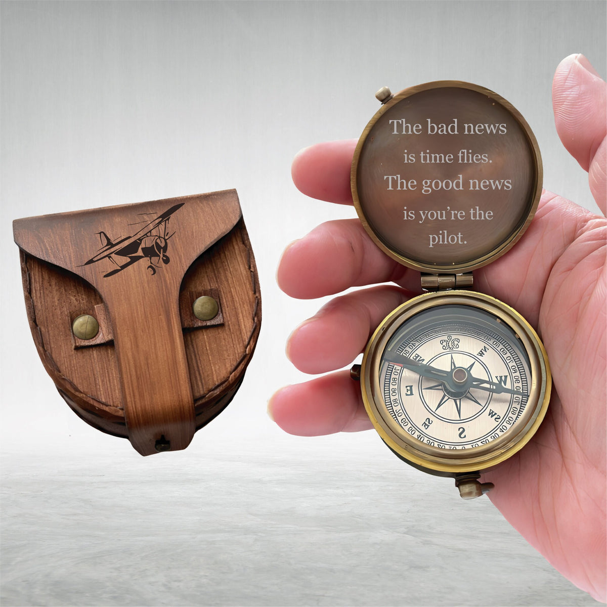 May include: A vintage brass compass with a leather case. The compass is open, revealing a directional dial and the quote, "The bad news is time flies. The good news is you're the pilot." The leather case features an engraved airplane.