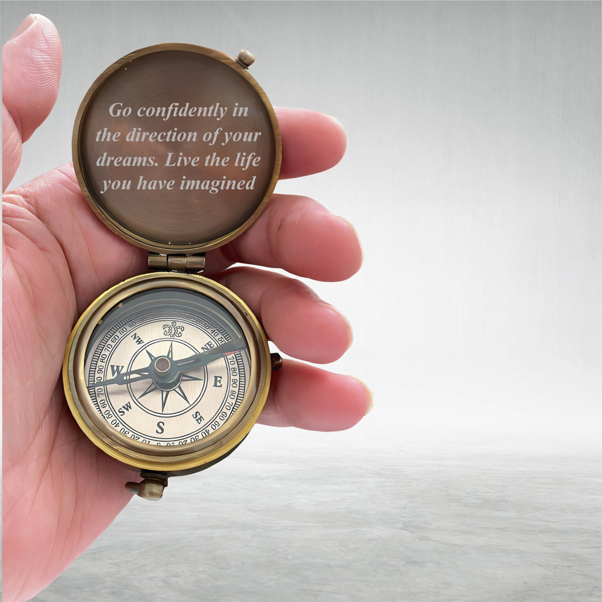 May include: A vintage brass compass held open, displaying the compass rose and the text "Go confidently in the direction of your dreams. Live the life you have imagined." The compass is in a person's hand.