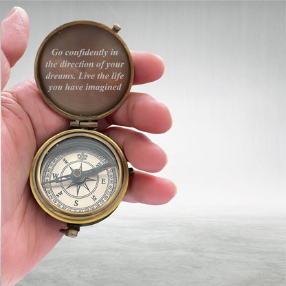 May include: A vintage brass compass held open, displaying the compass rose and the text "Go confidently in the direction of your dreams. Live the life you have imagined." The compass is in a person's hand.