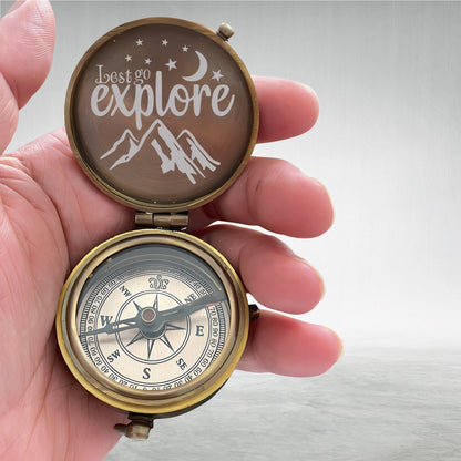 May include: A brass compass with a lid that has the words "Let's go explore" and a mountain range design. The compass face has a black needle and a white background with black markings.