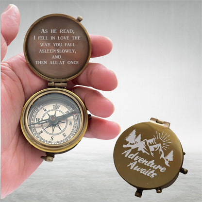May include: A brass pocket compass with a hinged lid. The interior lid is engraved with the text: AS HE READ, I FELL IN LOVE THE WAY YOU FALL ASLEEP: SLOWLY, AND THEN ALL AT ONCE. The exterior lid features an engraved mountain and tree scene with the text ADVENTURE AWAITS.