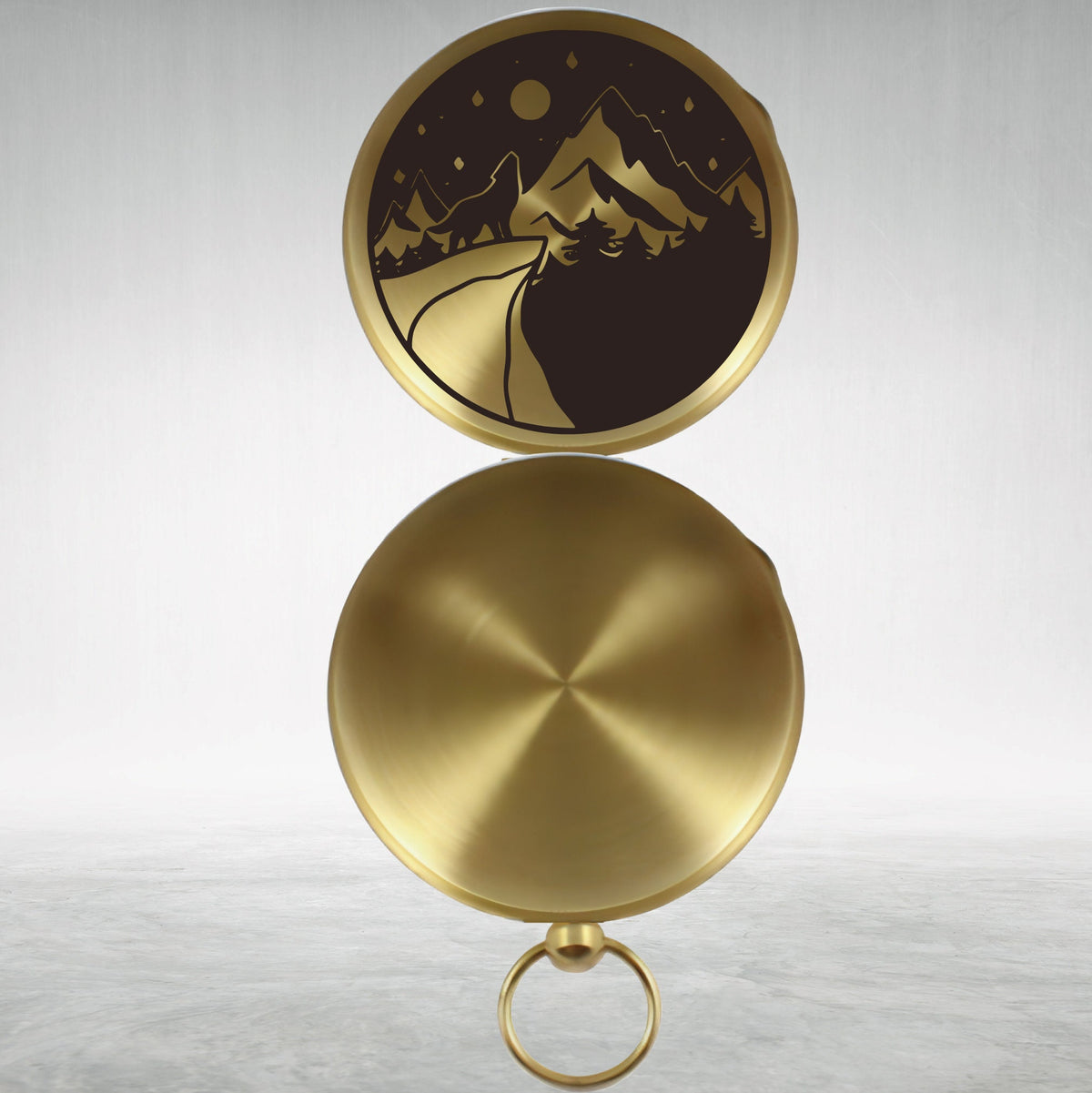 May include: A gold compass with a black and white design of a mountain range and a winding road. The compass has a clear glass cover and a metal ring.