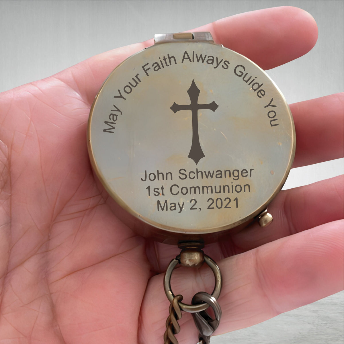 May include: A brass compass with a cross and the inscription "May Your Faith Always Guide You" and "John Schwanger 1st Communion May 2, 2021".