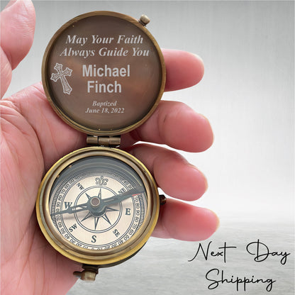 May include: A brass compass with a glass face and a compass needle. The lid of the compass is open and has an engraved message that reads "May Your Faith Always Guide You Michael Finch Baptized June 18, 2022".