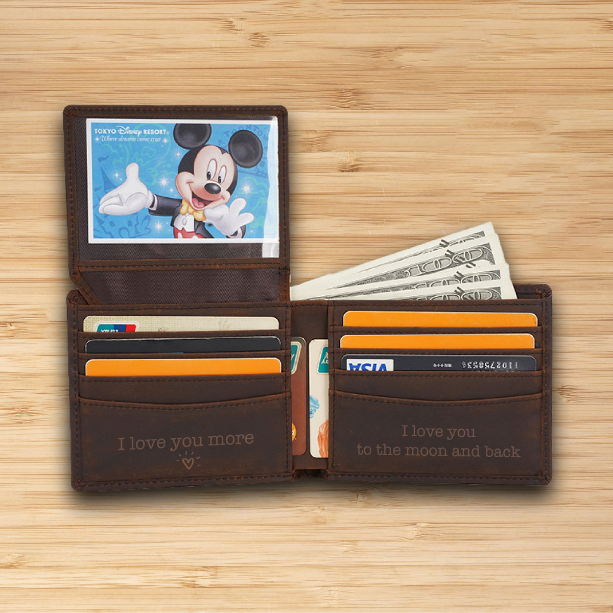 May include: A brown leather wallet with a Mickey Mouse image in the window. The wallet has multiple card slots and a cash pocket. The inside of the wallet is engraved with the text "I love you more" and "I love you to the moon and back".