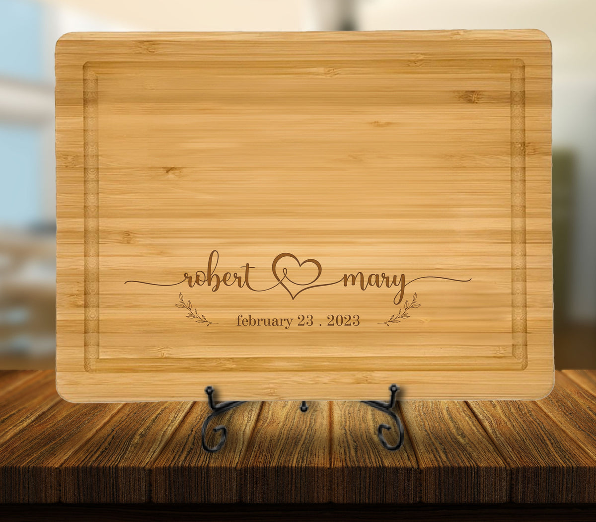 May include: A light brown bamboo cutting board with a personalized inscription. The inscription reads "robert & mary" with a heart symbol and the date "february 23, 2023".