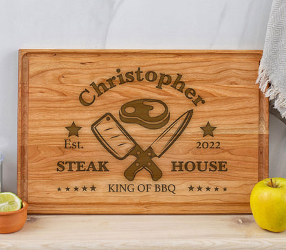 May include: A personalized wooden cutting board with the text "Christopher Steak House Est. 2022 King of BBQ" and a graphic of crossed knives and a steak.