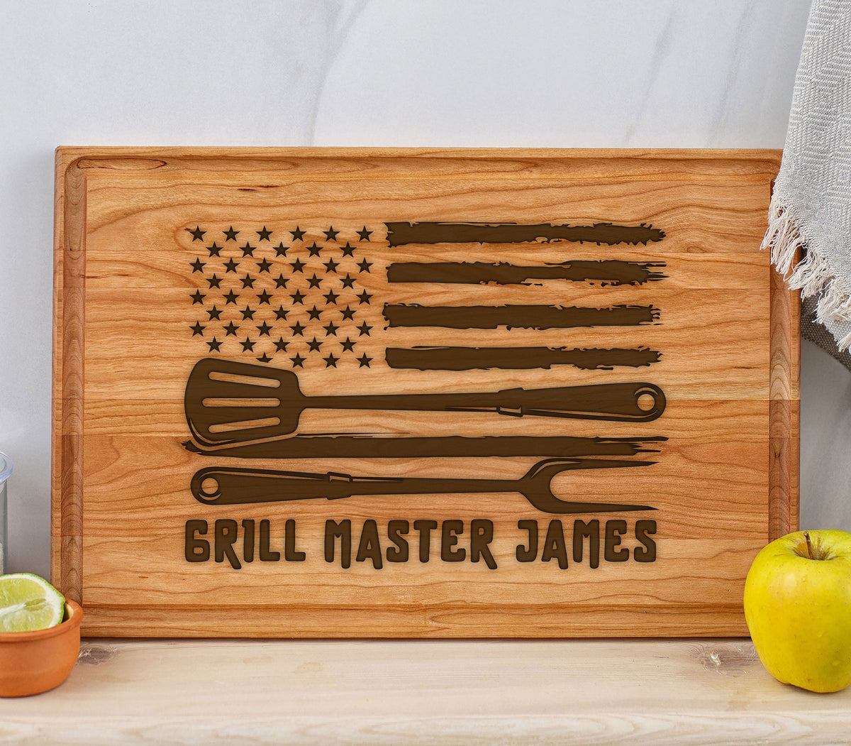May include: A wooden cutting board with a distressed American flag design, a spatula, tongs, and the text "Grill Master James".