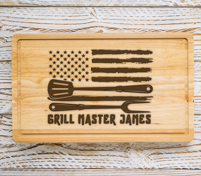 May include: Wooden cutting board with an American flag design, a spatula, a knife, and a grilling fork. The text "Grill Master James" is engraved on the board.