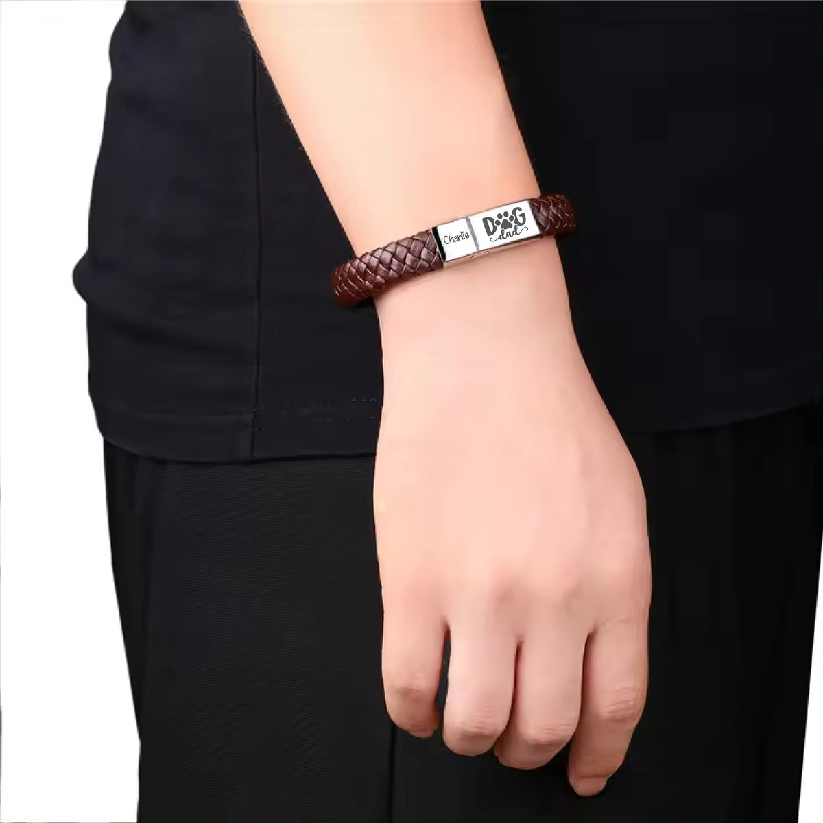 May include: A brown leather bracelet with a silver plate that reads "Dog Dad" with a paw print. 