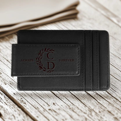 May include: Black leather wallet with a money clip. The wallet features the words "ALWAYS FOREVER" and the initials "C D" inside a decorative wreath. The wallet has card slots and is on a wooden surface.