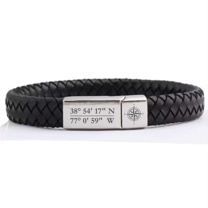 May include: Black leather bracelet with a silver metal plate engraved with the coordinates 38° 54' 17" N 77° 0' 59" W and a compass design.