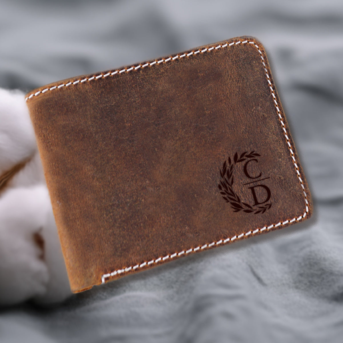 May include: A brown leather wallet with white stitching and a monogrammed design. The monogram is a wreath with the letters "C" and "D" inside.
