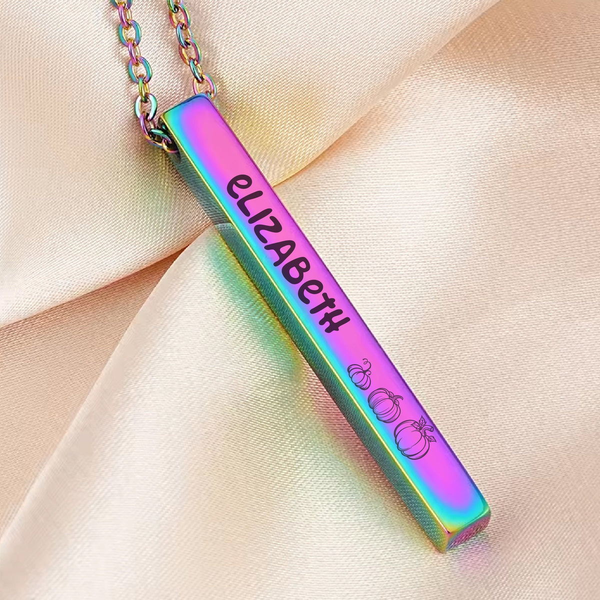 May include: A rainbow iridescent bar necklace with the name "Elizabeth" engraved on it and a small pumpkin design at the bottom.
