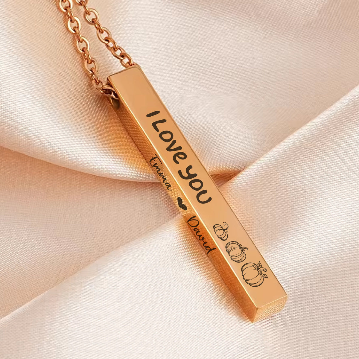 May include: Gold bar necklace with the words "I Love You" engraved on one side and the names "Emma" and "David" with a heart and pumpkins engraved on the other side.
