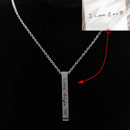 May include: A silver necklace with a vertical bar pendant engraved with the words "Love Adele" and an infinity symbol.
