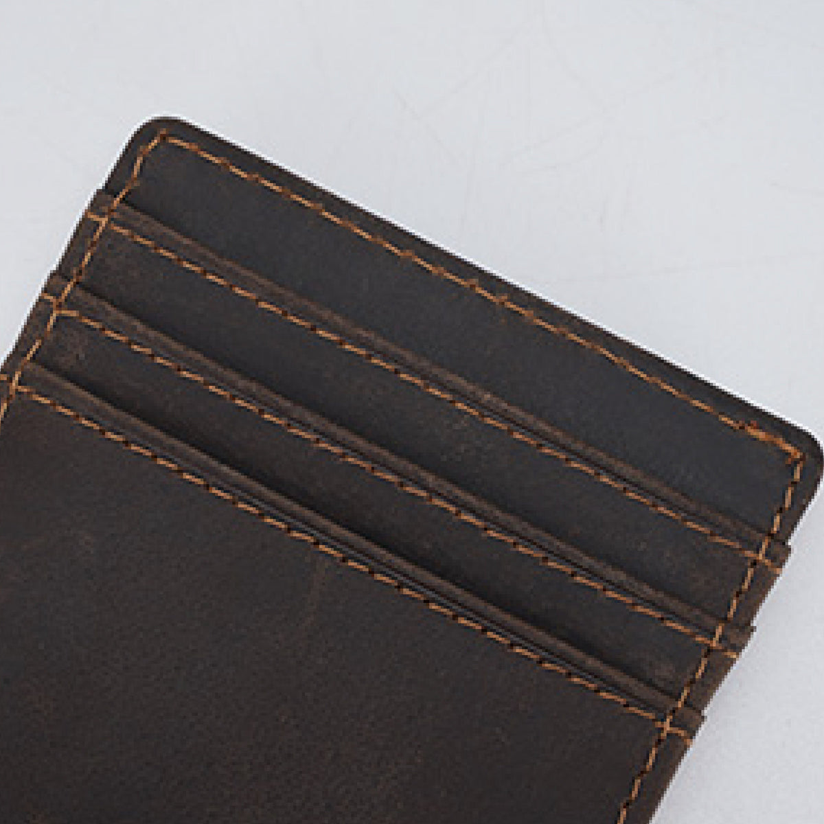 May include: A close-up of a dark brown leather cardholder with four card slots. The edges are rounded, and the stitching is a contrasting tan color. The leather has a slightly distressed appearance.
