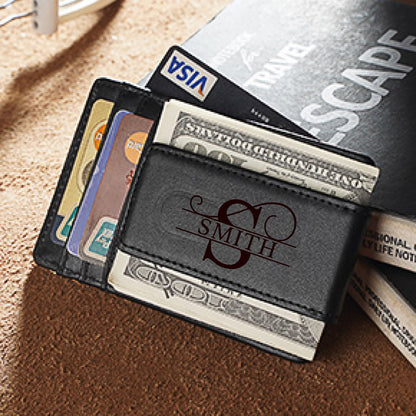 May include: Black leather money clip with the name "SMITH" and the letter "S" engraved in a decorative font. The clip holds several one-hundred-dollar bills, credit cards, and a Visa card. The background is a textured brown surface.