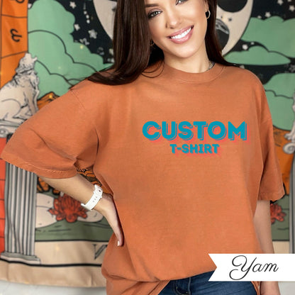 May include: An orange t-shirt with the words "CUSTOM T-SHIRT" in blue and red. The shirt is a solid color and has short sleeves. The model is wearing a white watch.