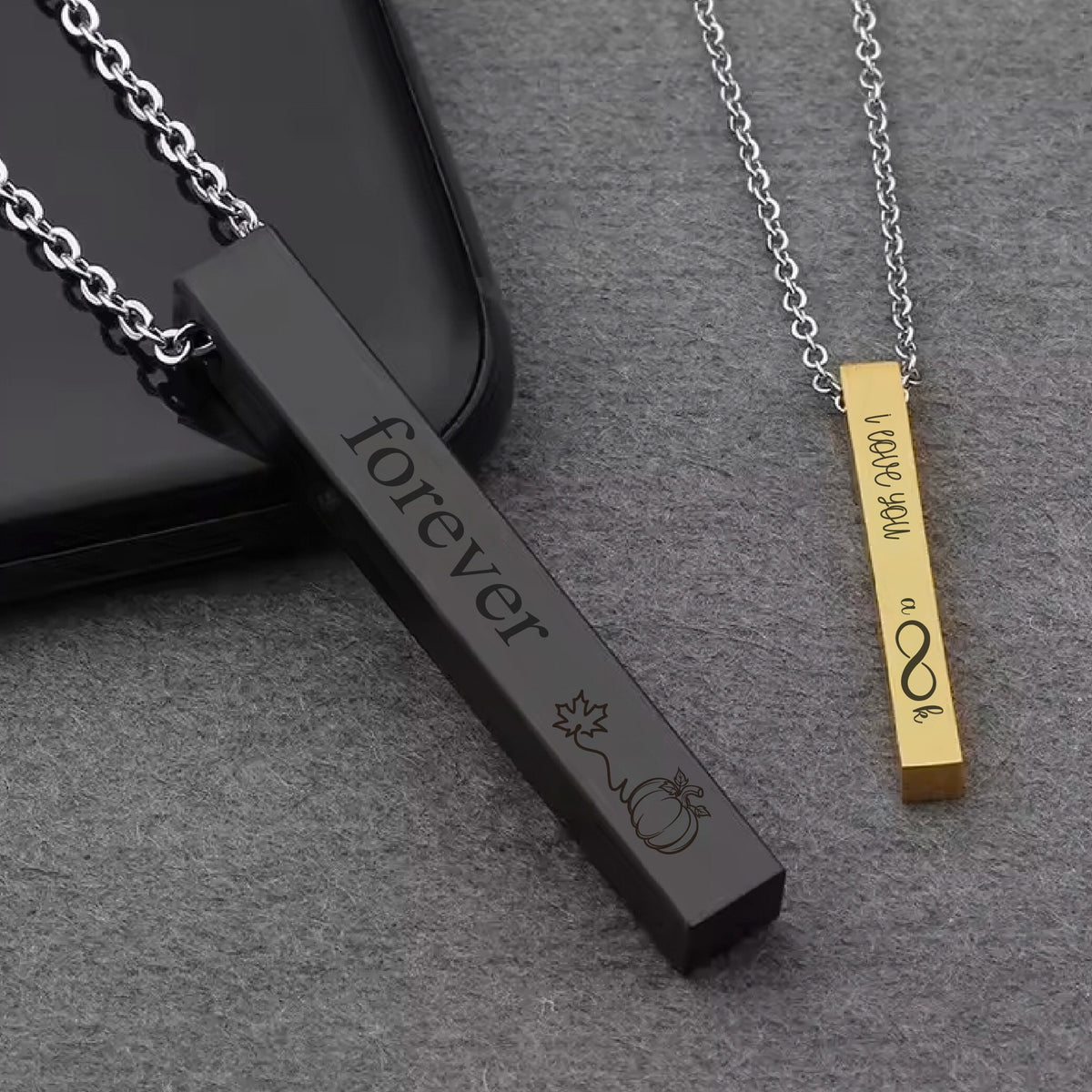 May include: Two bar necklaces with engraved messages. One black bar necklace says "forever" with a pumpkin and leaf design. The other gold bar necklace says "I love you a lot" with an infinity symbol.