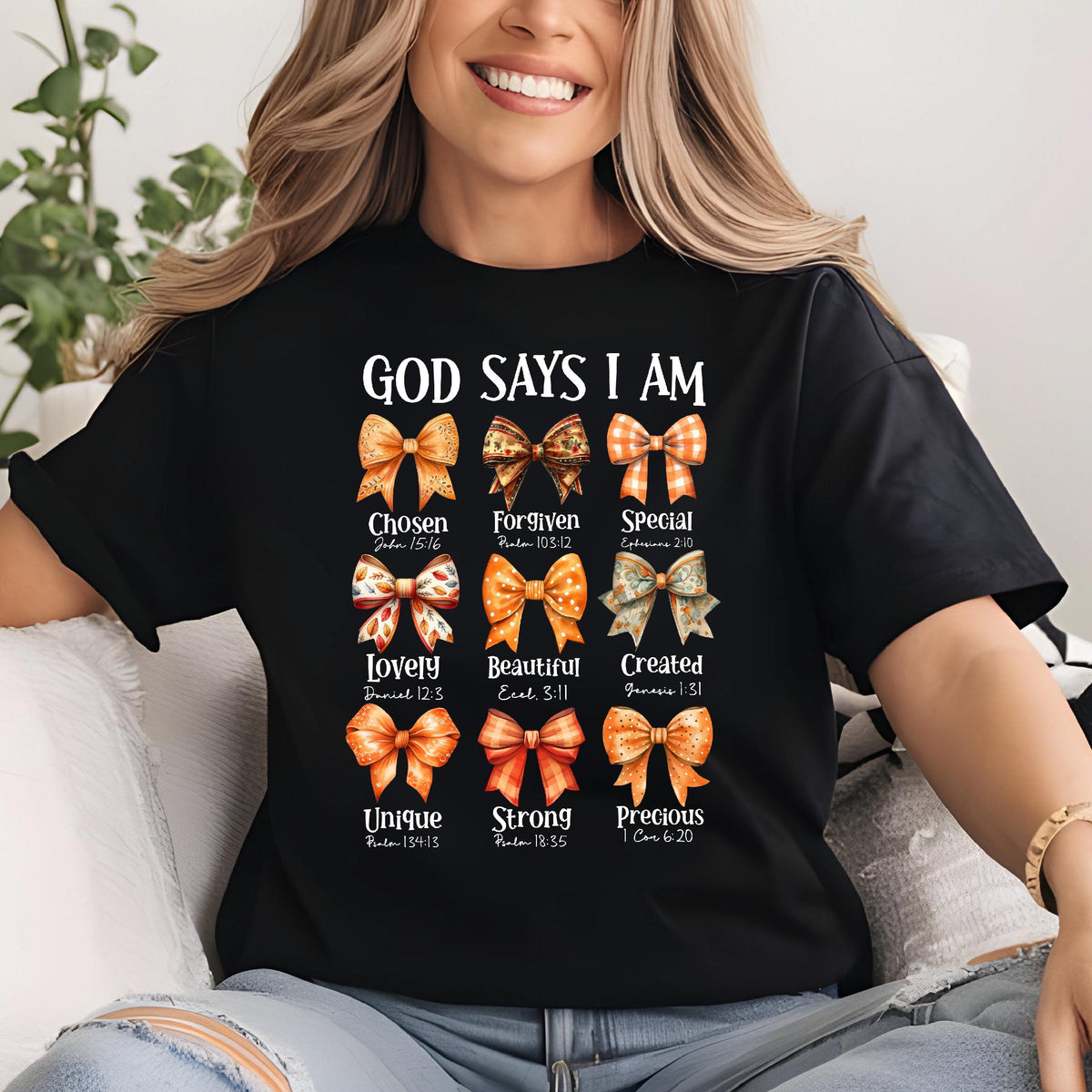 May include: A black t-shirt featuring the text GOD SAYS I AM above nine illustrated bows in shades of orange, brown, and cream. Each bow is labeled with a word and a Bible verse, including Chosen, Forgiven, Special, Lovely, Beautiful, Created, Unique, Strong, and Precious.