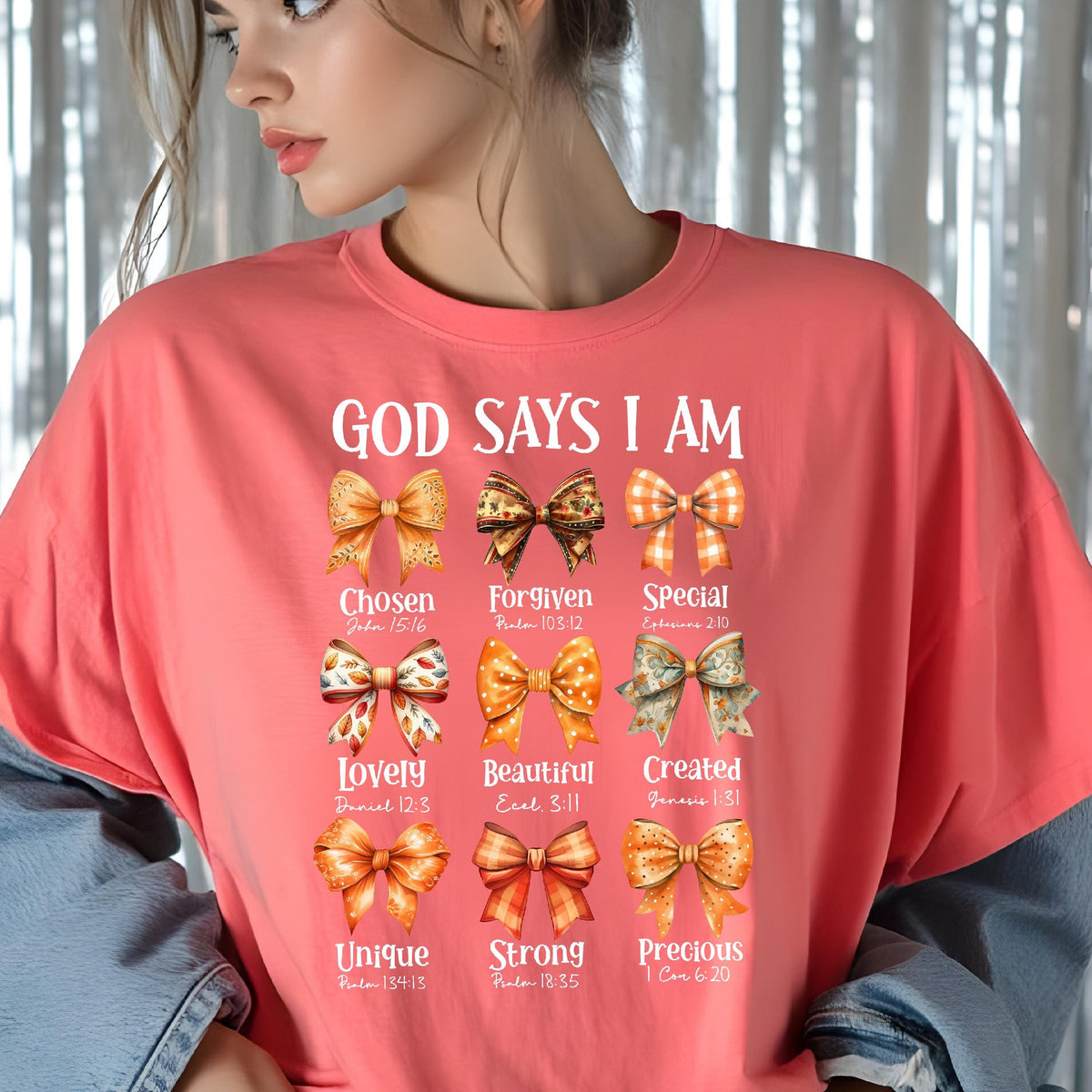 May include: A coral-colored t-shirt featuring the text "GOD SAYS I AM" above nine distinct illustrated bows in shades of orange, gold, and brown. Each bow is paired with a descriptive word and a Bible verse reference, including Chosen, Forgiven, Special, Lovely, Beautiful, Created, Unique, Strong, and Precious.