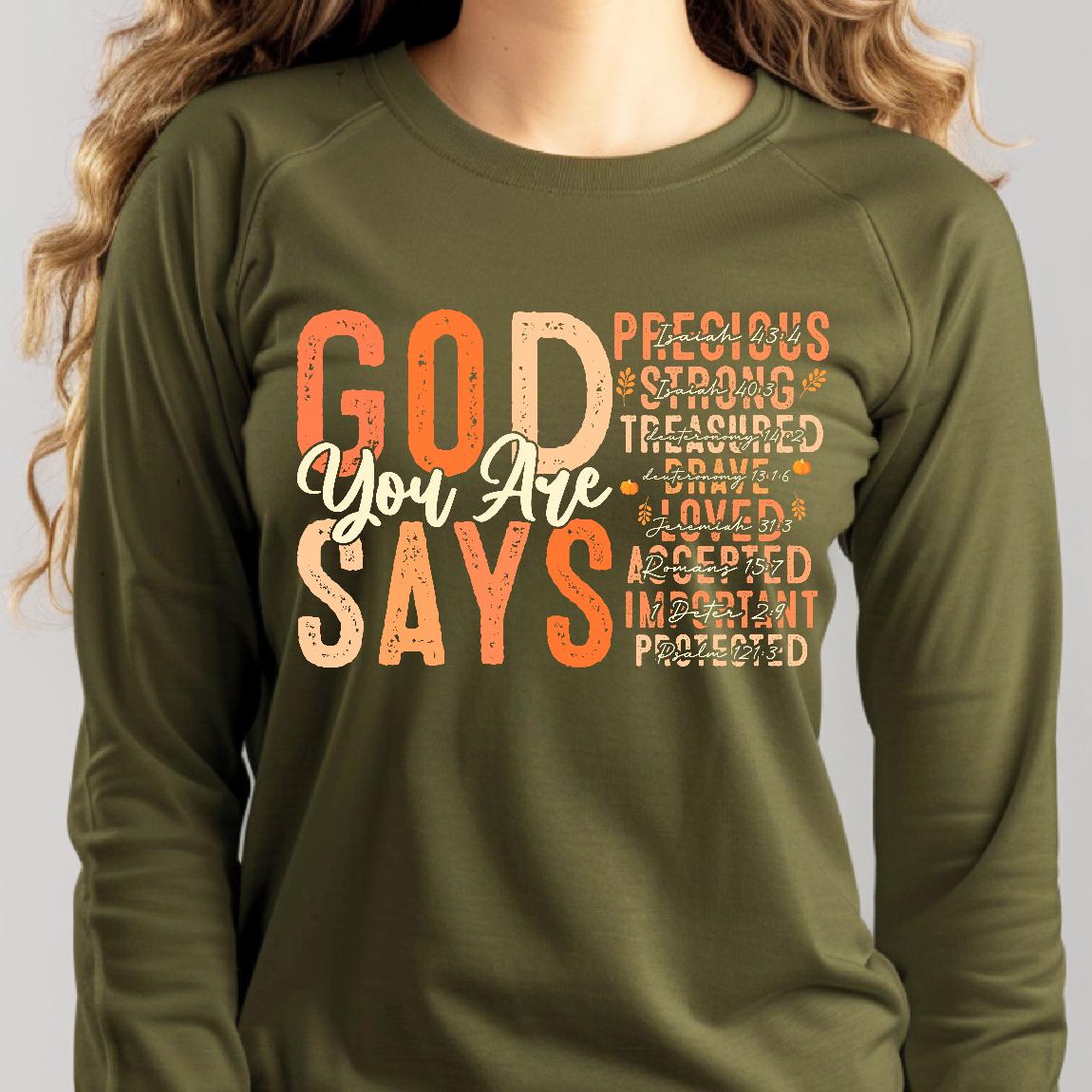 May include: A green long-sleeved shirt with the text "GOD You Are SAYS" in orange and pink letters. The text is surrounded by smaller text in a similar color scheme, including the words "Precious", "Strong", "Treasured", "Brave", "Loved", "Accepted", "Important", and "Protected".