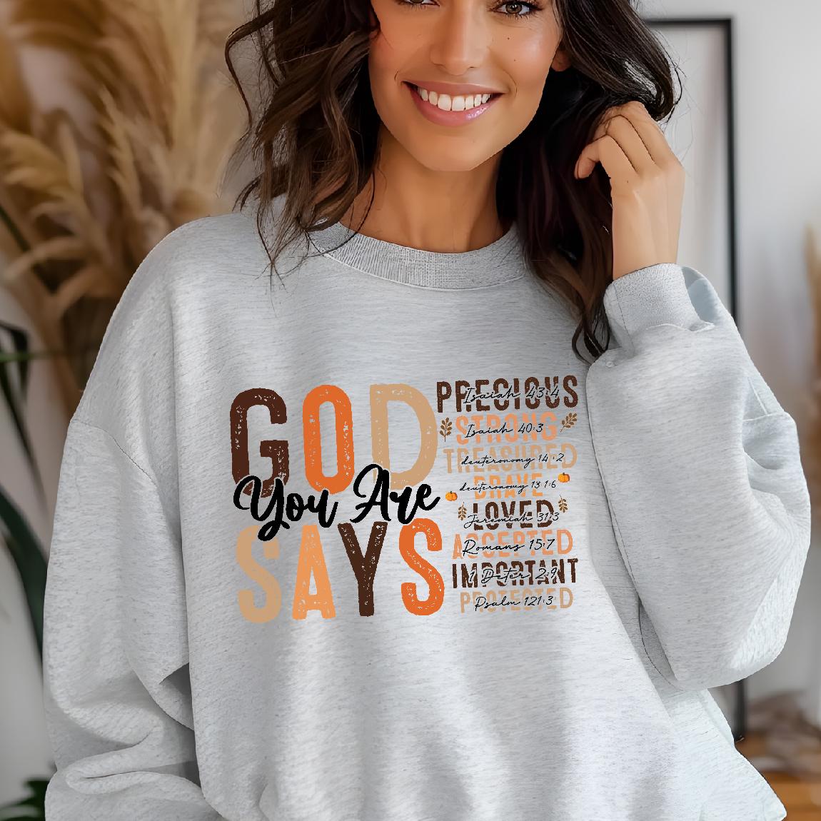 May include: A gray sweatshirt with a graphic print that says "GOD SAYS YOU ARE" in brown and orange letters. The graphic also includes bible verses in smaller font.