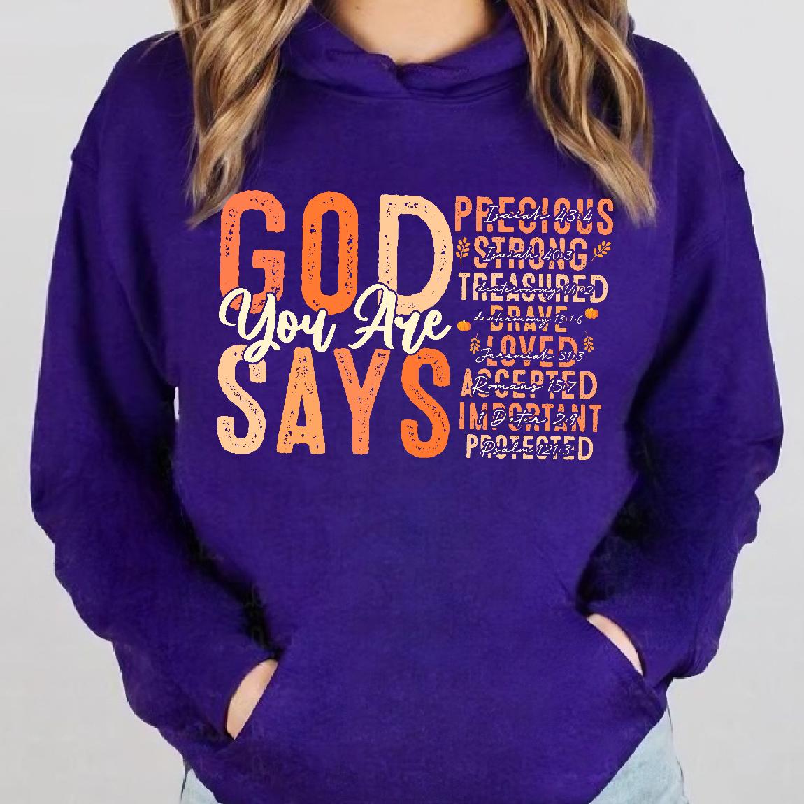 May include: Purple hoodie with a graphic print that says "God You Are Says" with a list of positive affirmations in orange and white text. The affirmations include "Precious", "Strong", "Treasured", "Brave", "Loved", "Accepted", "Important", and "Protected".