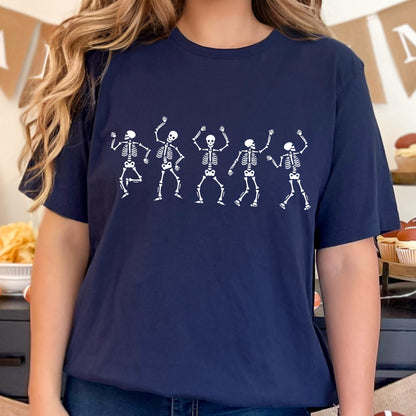 May include: Navy blue t-shirt featuring a white graphic of five dancing skeletons. The skeletons are in various poses with their arms raised. The shirt is a comfortable, casual style, perfect for Halloween or a fun, spooky event.
