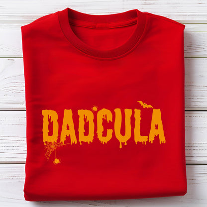 May include: A bright red crew neck t-shirt featuring the orange text DADCULA in a dripping, horror-inspired font. The design includes a small orange spider hanging from a web on the left side, a tiny spider above the letters, and a bat.