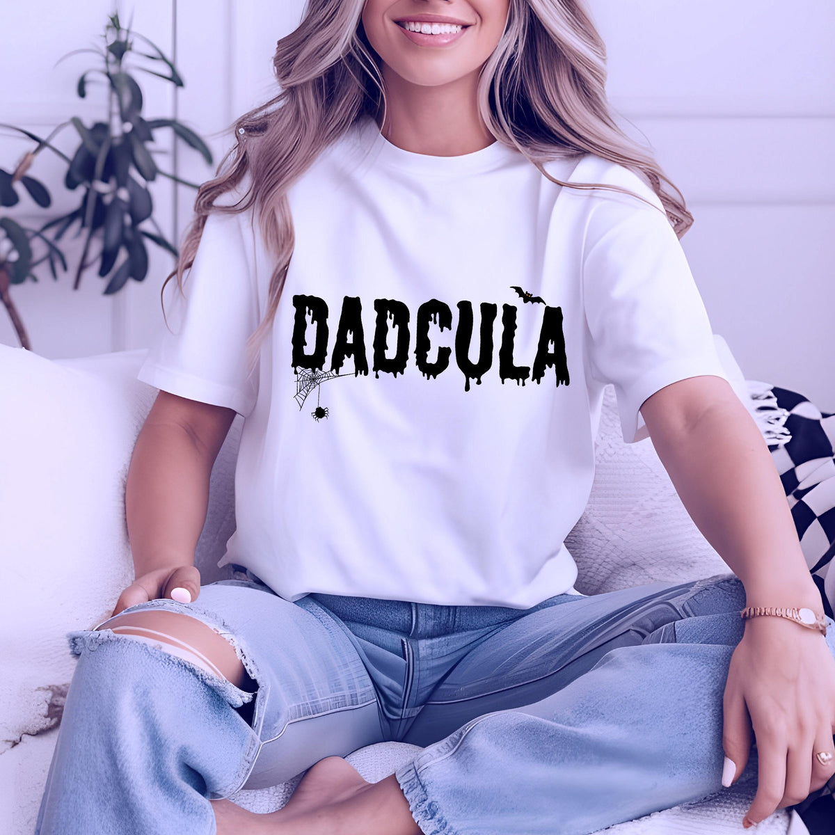 May include: A white short-sleeved t-shirt featuring the black text DADCULA in a dripping, horror-inspired font. The design includes a small black spider hanging from a web on the letter D and a small black bat silhouette above the letter A.