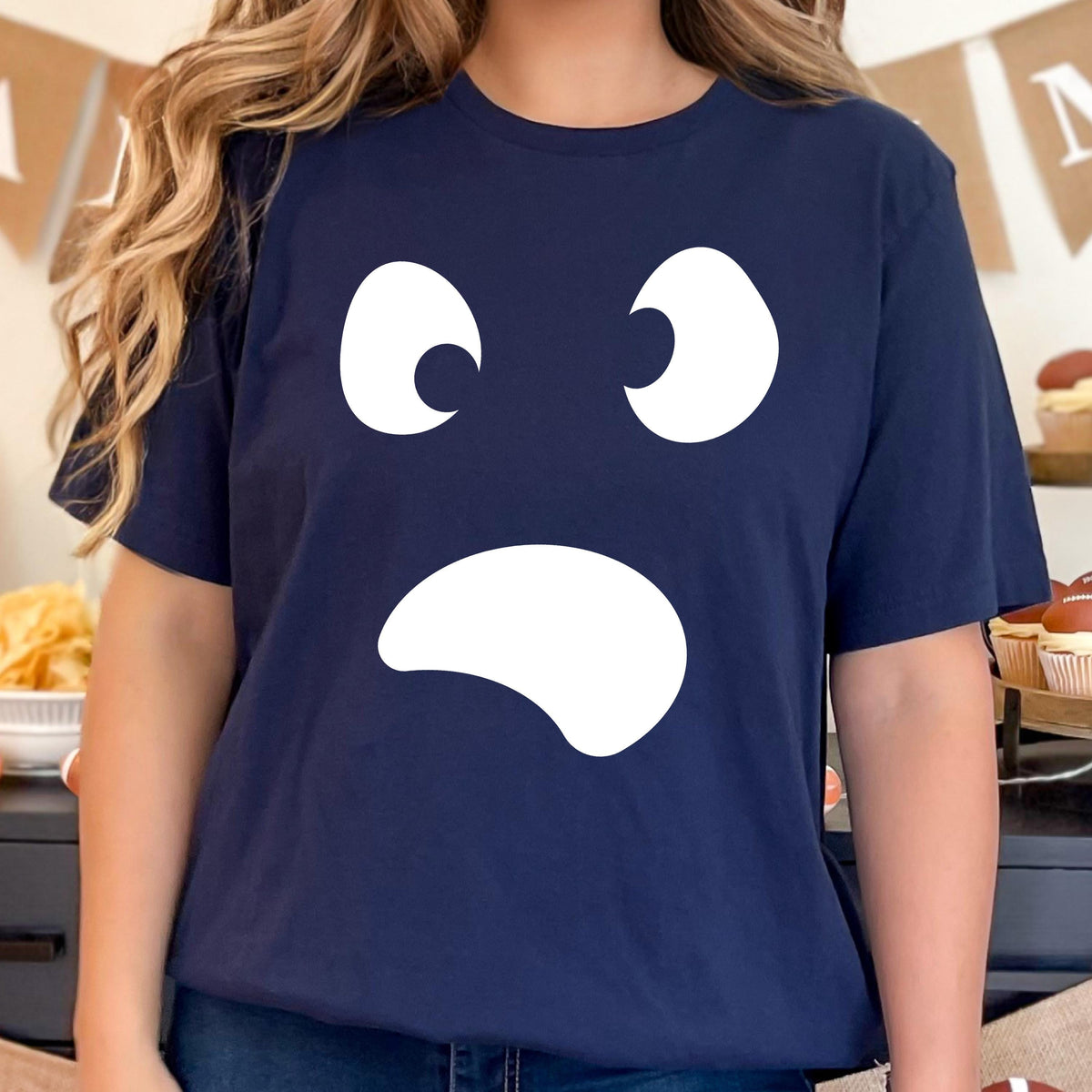 May include: Navy blue t-shirt featuring a white ghost face design. The graphic includes two curved eyes and a curved mouth, creating a simple, yet expressive design. The shirt is a comfortable, casual style.