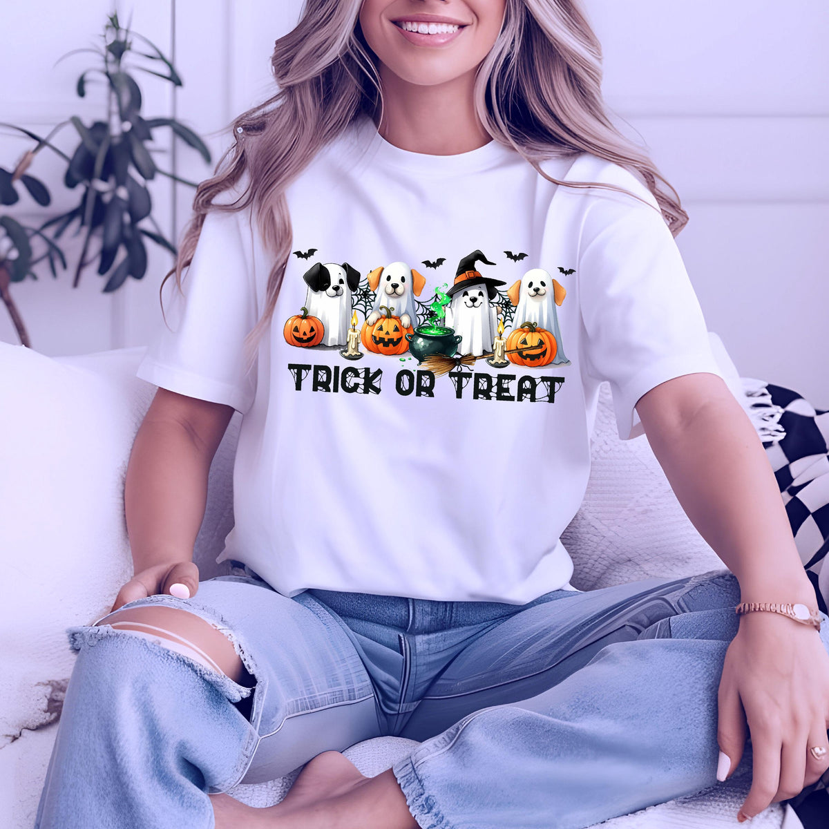 May include: A white t-shirt featuring a graphic of four dogs dressed as ghosts, sitting behind orange pumpkins and a green bubbling cauldron. The text TRICK OR TREAT is printed in black below the dogs, accompanied by small black bats and spiderwebs.