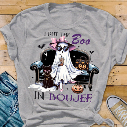 May include: A heather gray t-shirt featuring a graphic of a ghost wearing a pink bow, hat, and sunglasses, sitting on a black sofa with a black cat, a pumpkin, and a handbag. The text reads I PUT THE BOO IN BOUJEE in purple and black lettering.