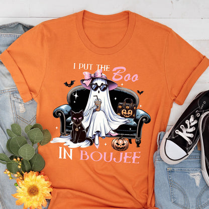May include: An orange t-shirt featuring a graphic of a ghost wearing a pink bow and sunglasses, sitting on a black sofa with a black cat, a pumpkin-patterned handbag, and a coffee cup. The text reads I PUT THE BOO IN BOUJEE with small bats.