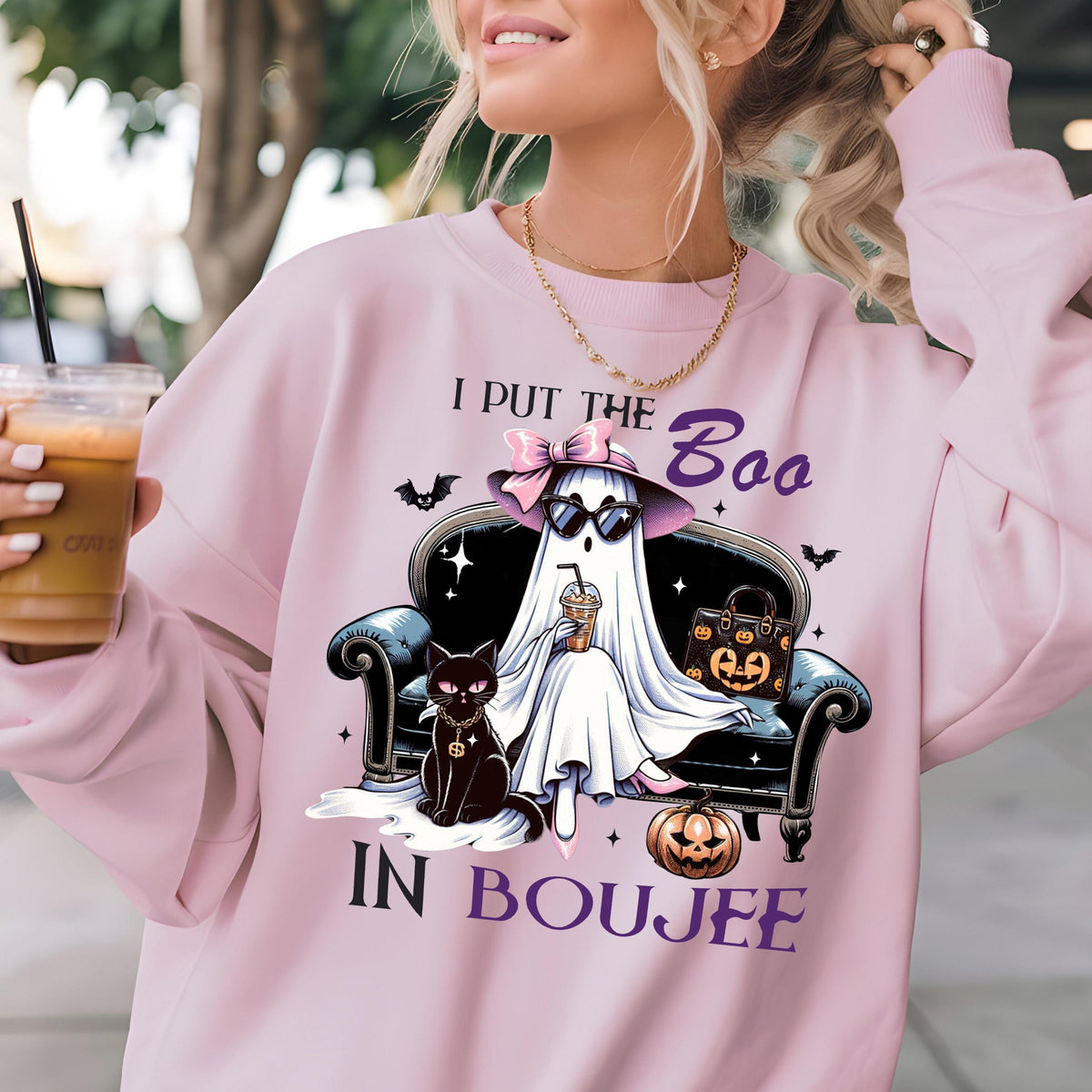 May include: A light pink sweatshirt featuring a graphic of a ghost wearing a hat and sunglasses, sitting on a sofa with a black cat, a pumpkin, and a handbag. The text reads I PUT THE Boo IN BOUJEE, surrounded by small bats and stars.