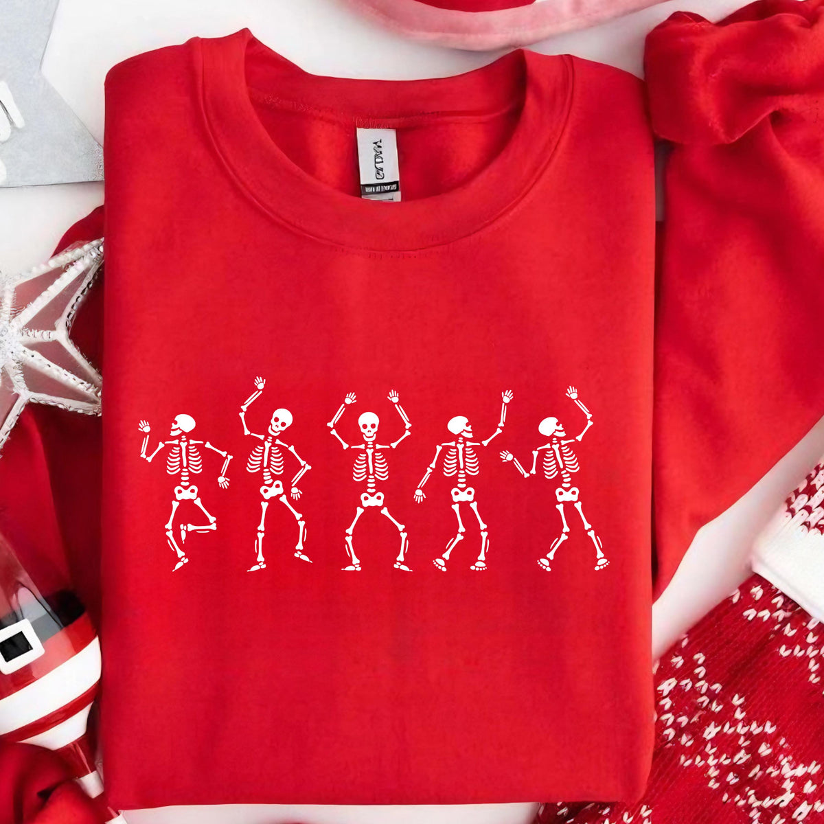 May include: A red crewneck sweatshirt featuring a white graphic of five dancing skeletons. The skeletons are in various poses with their arms raised. The sweatshirt is made of a soft material and is perfect for Halloween or any spooky occasion.