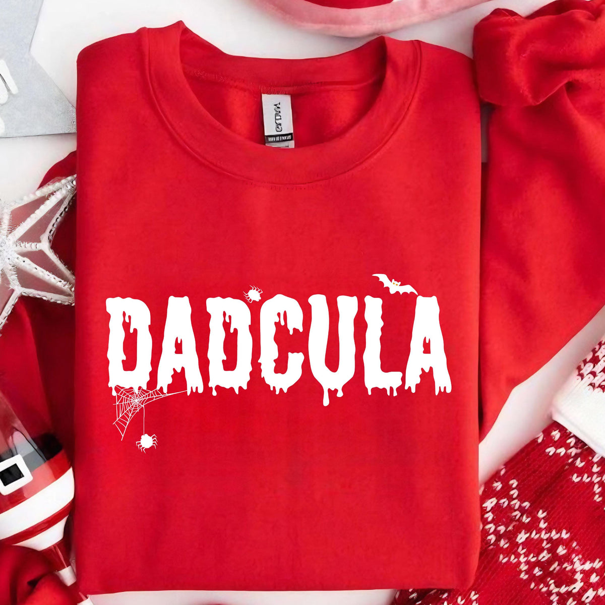 May include: Red sweatshirt with white text that reads "DADICULA" in a dripping font. The text is surrounded by a spider web and bats.