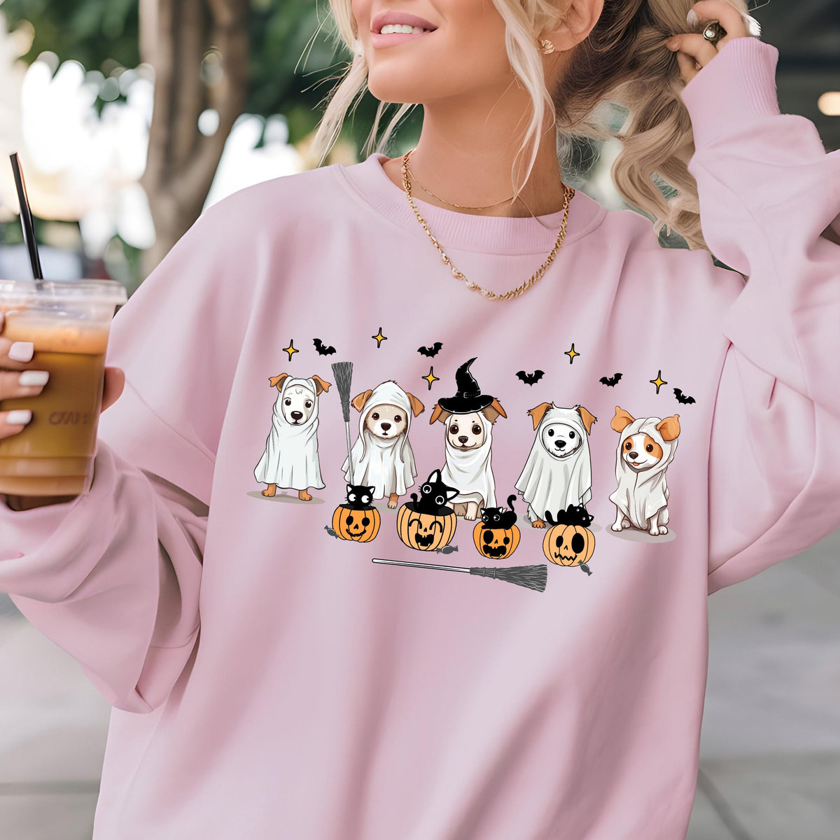 May include: A light pink sweatshirt featuring a Halloween-themed design. The graphic includes cartoon dogs dressed as ghosts, a witch, and bats, along with pumpkins and a broom. The sweatshirt has a crew neck.