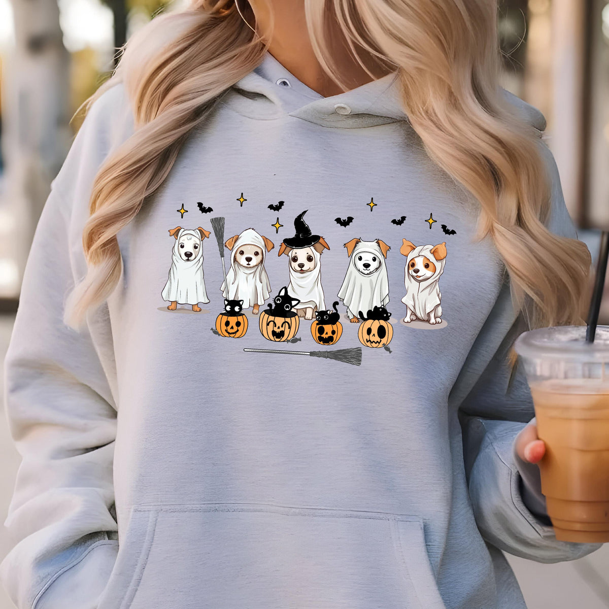May include: A light gray hoodie featuring a Halloween-themed graphic. The graphic depicts six dogs dressed in costumes, including ghosts and witches, with pumpkins, bats, and stars. A broom is also included in the design.