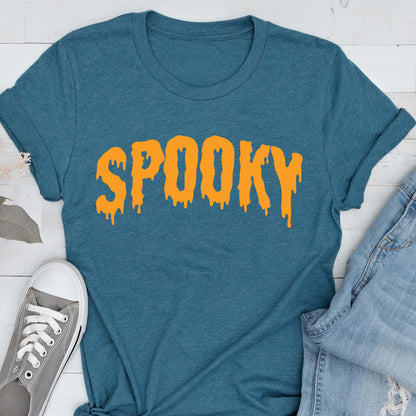 May include: Teal t-shirt with the word "SPOOKY" in orange, dripping letters. The shirt is paired with blue jeans and gray sneakers, suggesting a casual, Halloween-themed outfit. The design is simple and eye-catching.