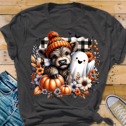 May include: A charcoal gray t-shirt featuring a graphic of a fluffy Highland cow wearing an orange knit beanie, standing next to a white ghost. The design includes orange pumpkins, autumn flowers, and a black and white buffalo plaid background.