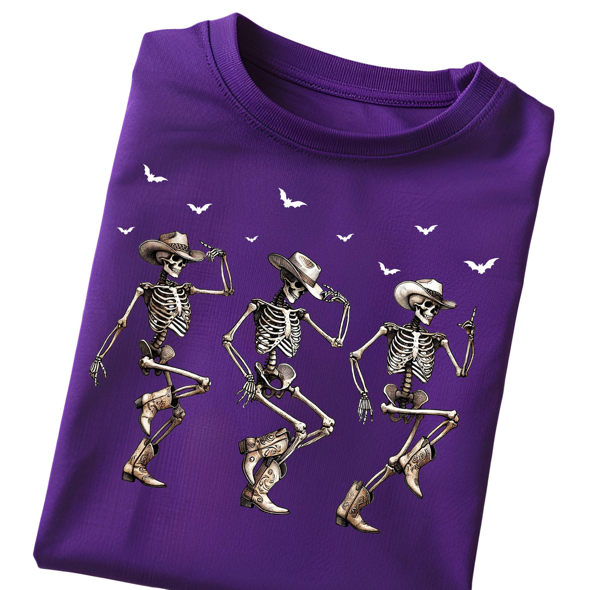 May include: A purple t-shirt featuring three dancing skeletons wearing cowboy hats and boots. White bat silhouettes are scattered across the top. The skeletons are in various dance poses, with detailed bone structures.