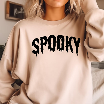 May include: A beige crewneck sweatshirt featuring the word SPOOKY printed in a black, dripping, liquid-style font across the chest. The garment has long sleeves, a ribbed neckline, and a relaxed fit, providing a simple and clean aesthetic.