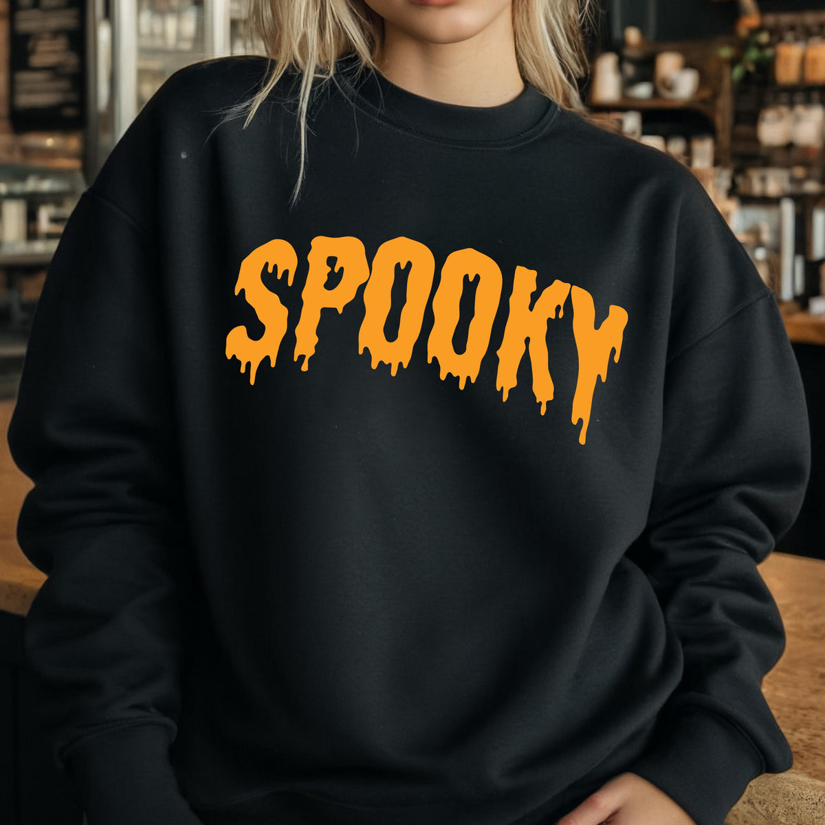 May include: A black long-sleeve crewneck sweatshirt featuring the word SPOOKY printed in a bright orange, dripping, liquid-style font across the chest. The garment has a standard fit with ribbed cuffs and a ribbed neckline, made of solid fabric.