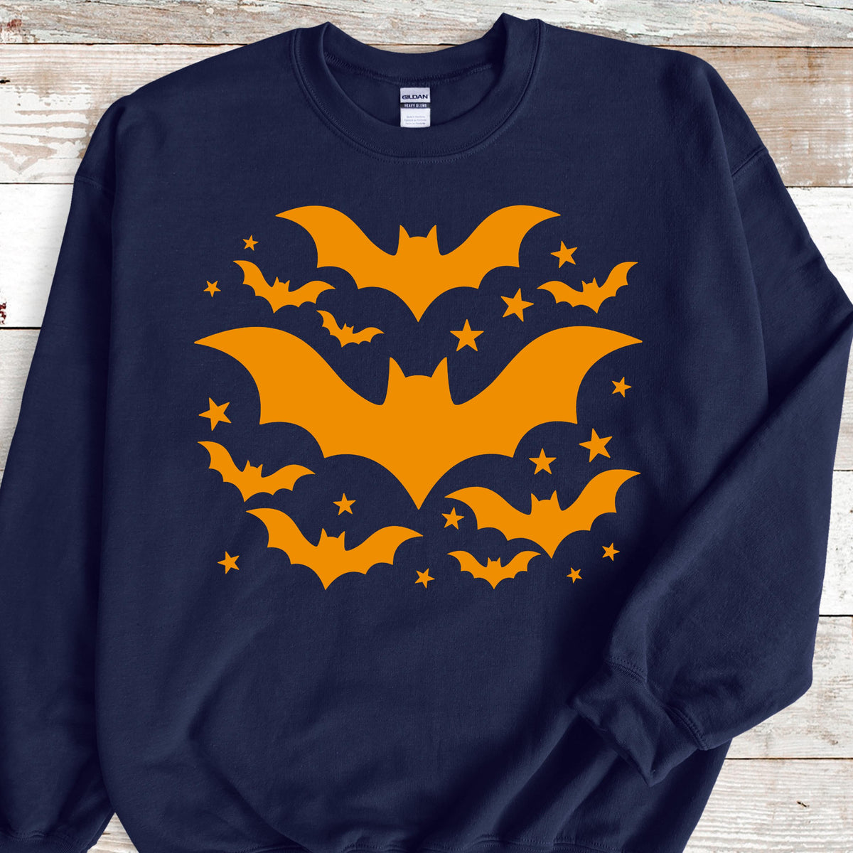 May include: Navy blue sweatshirt featuring a Halloween design. The design includes orange bats and stars arranged in a circular pattern. The bats vary in size, with several smaller bats surrounding larger ones. A festive and seasonal apparel item.