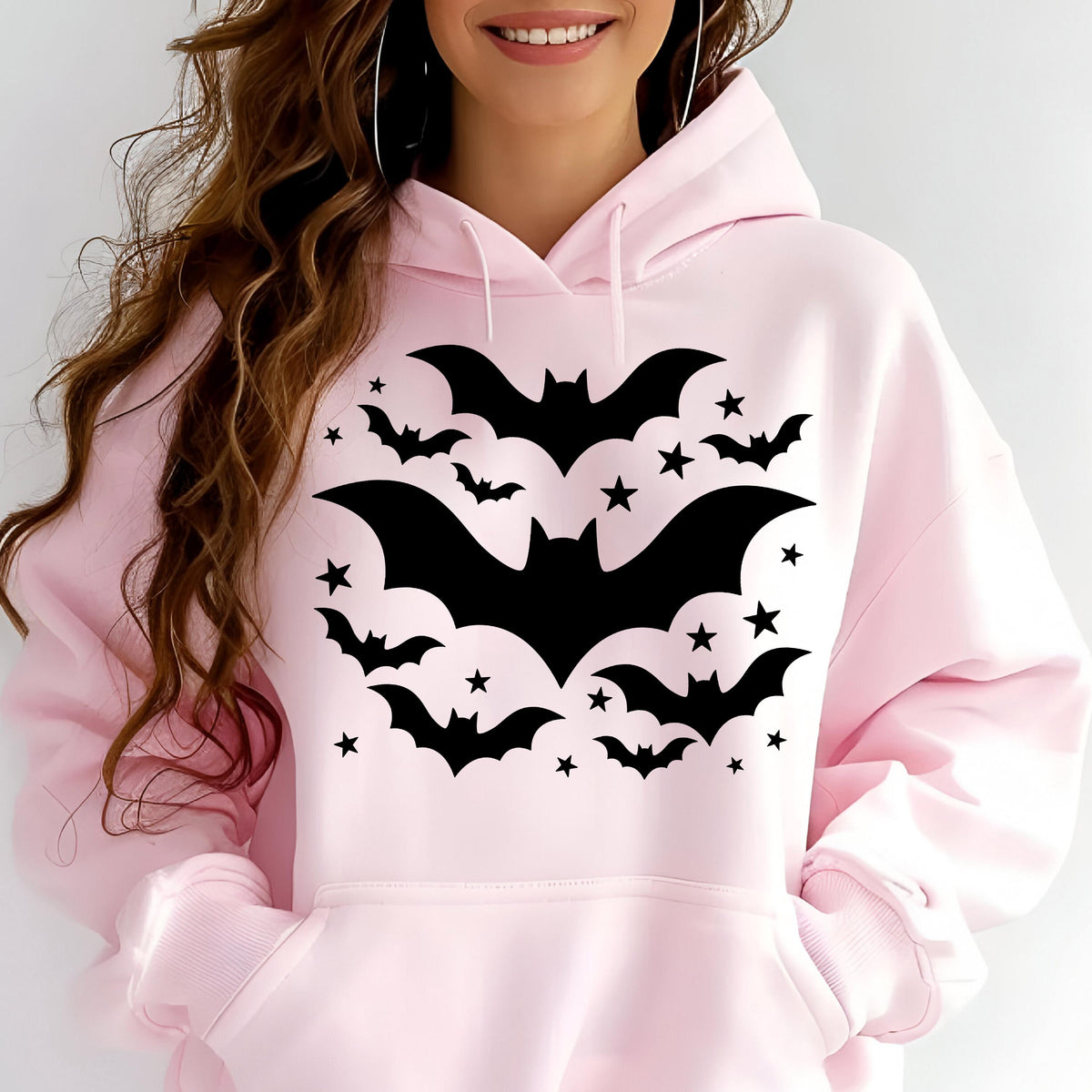 May include: A light pink hoodie featuring a black bat and star design. The graphic includes several bats of varying sizes and numerous stars, creating a Halloween or gothic theme. The hoodie has a drawstring hood and a front pocket.