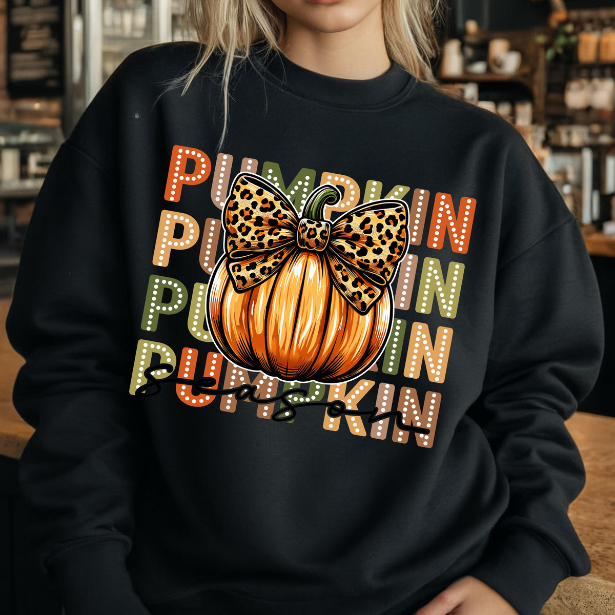 May include: Black sweatshirt featuring a large orange pumpkin with a leopard print bow. The word "PUMPKIN" is stacked vertically in orange, green, and brown dotted letters, creating a fall-themed design.